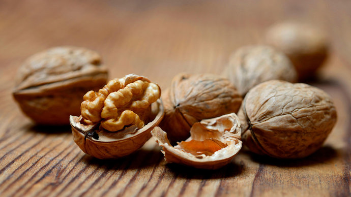 Walnuts with one cracked open on a wooden surface