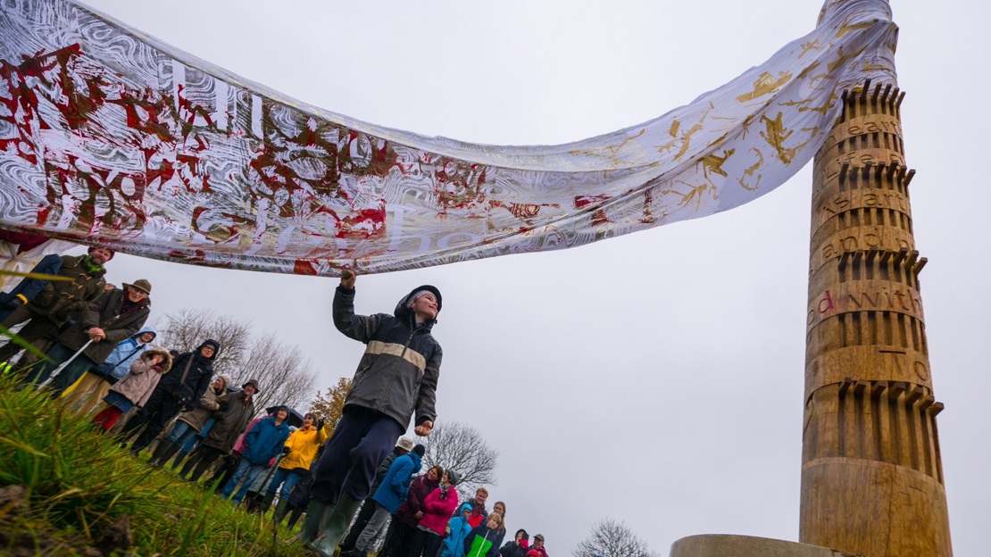 Boy holds long floating fabric draped from charter pole as crowd looks on