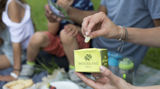 Woman putting a pound into a Woodland Trust donation box at a picnic