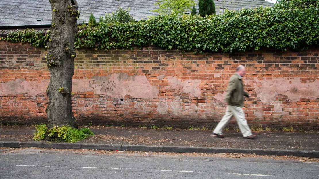 Man walking along pavement with street tree