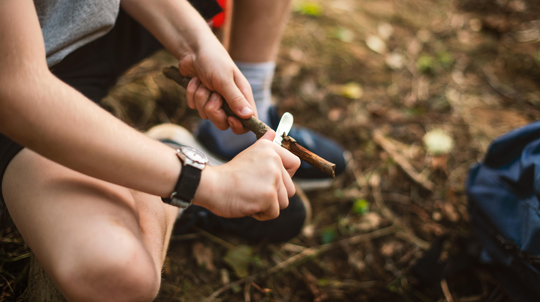Boy sat on floor whittling a stick with a knife