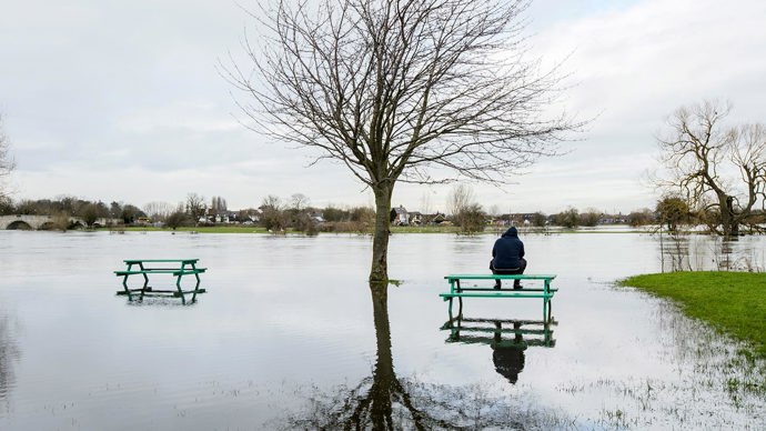 Man sat on picnic bench in park flooded by River Thames, Chertsey, Surrey.