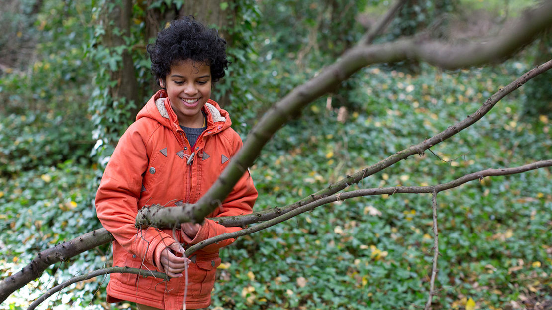 Smiling child collecting sticks while playing in Hainault Forest
