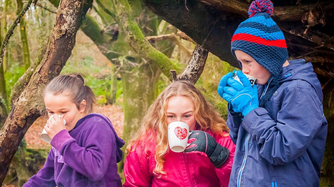 Three kids drinking from mugs in the woods