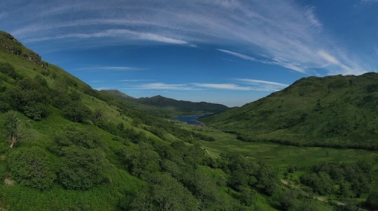 Landscape view of lush green mountains with a lake in the distance under a blue sky