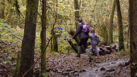 Mother and daughter stepping over stream wearing wellies