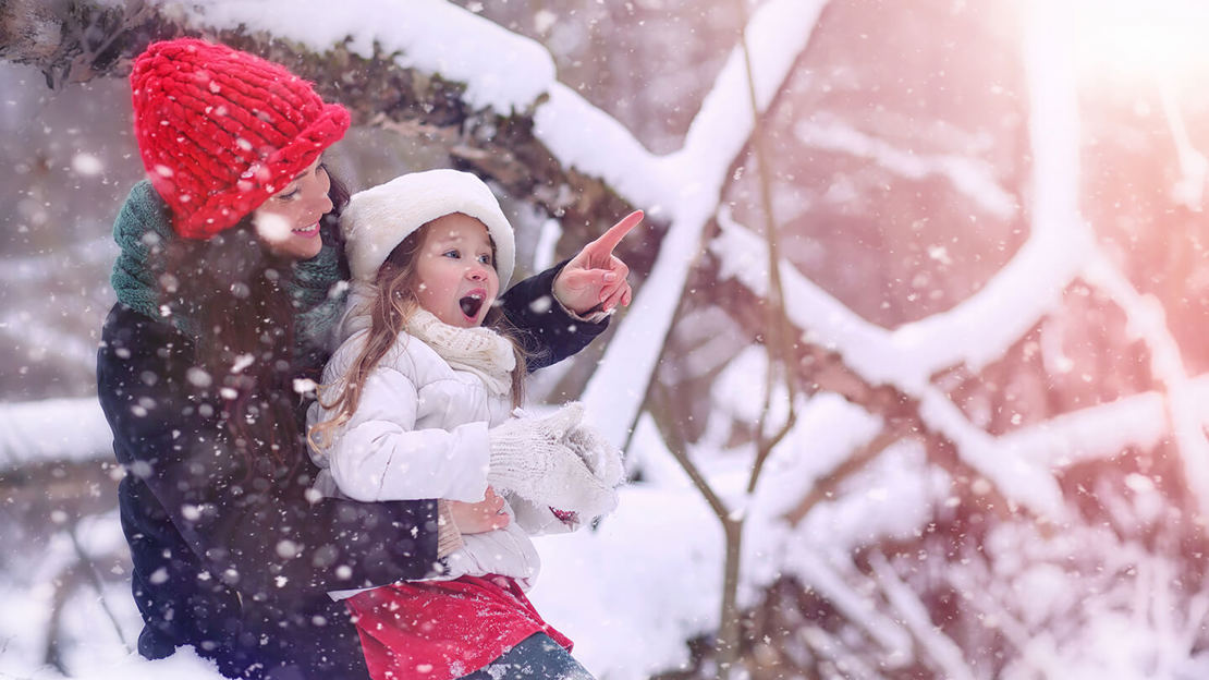 Smiling mother pointing something out to her excited daughter in a snowy forest