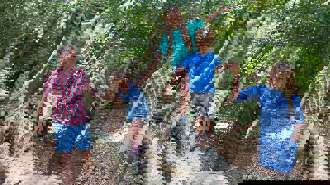 Family walking along a fallen tree in a summer woodland