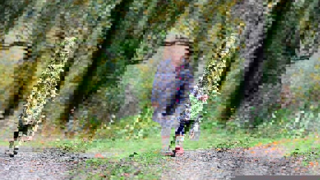 Young girl in coat and wellies holding a sapling while walking outdoors