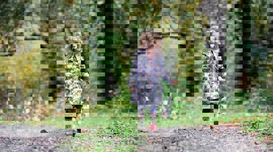 Young girl in coat and wellies holding a sapling while walking outdoors