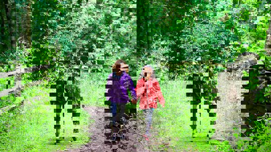 Two smiling girls walking through a summer woodland