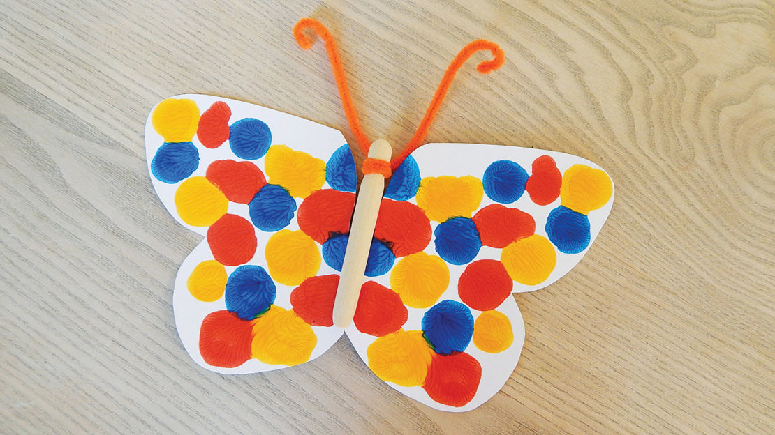 Bright butterfly symmetry painting in red, yellow and blue with orange antennae made form pipe cleaners