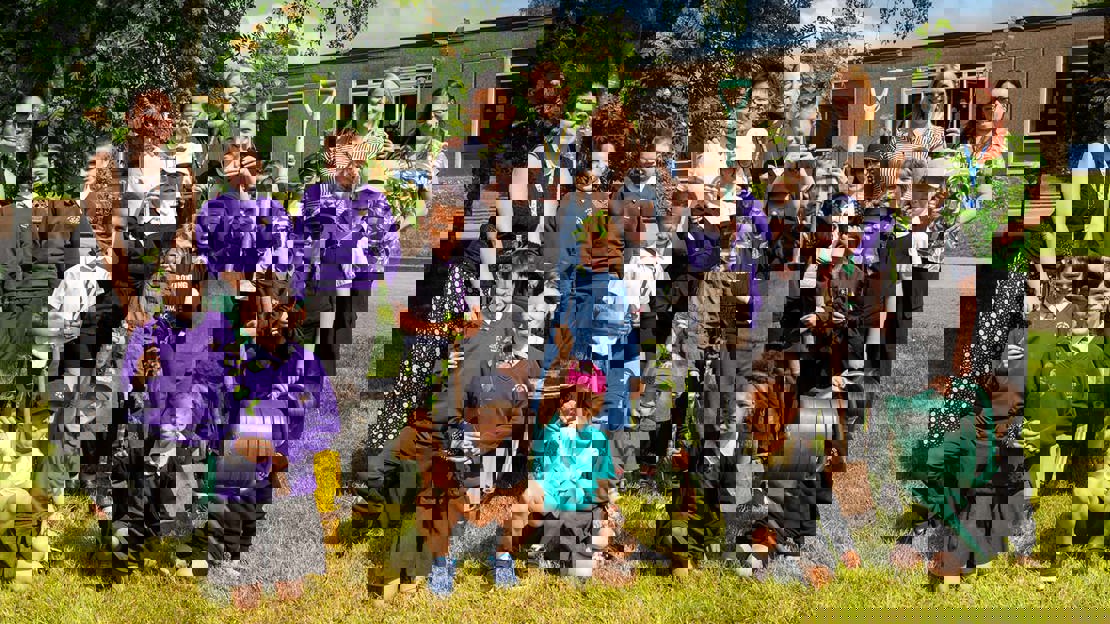 A group of smiling children and staff holding saplings in their schools grounds
