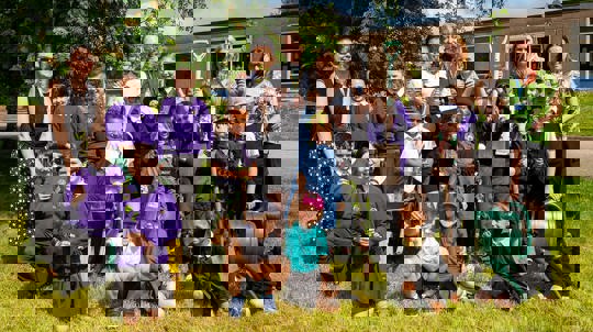 A group of smiling children and staff holding saplings in their schools grounds