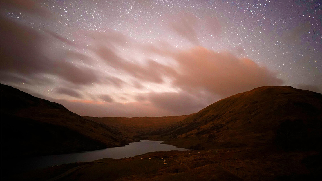 Stars in the night sky over hills and a lake