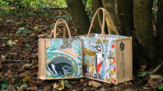 Two jute bags on top of leaf litter. One has a badger on it and one has a great spotted woodpecker on it.
