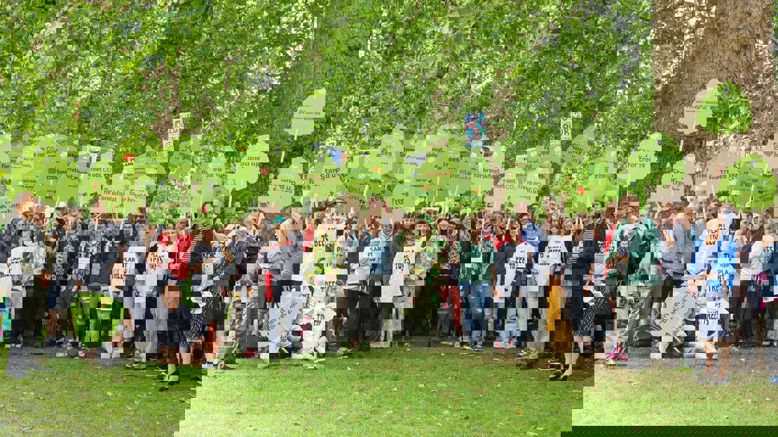 Several people gathered under a tree holding placards and wearing 'Plant trees' T-shirts
