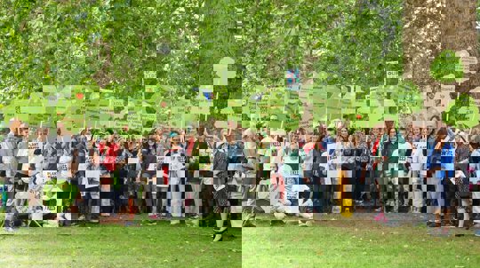 Several people gathered under a tree holding placards and wearing 'Plant trees' T-shirts