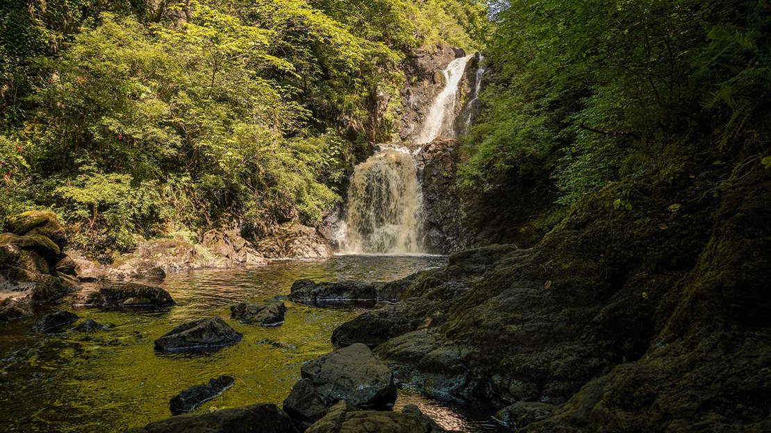 Water tumbling down a two-tier waterfall at Uig Wood into a rocky pool below.