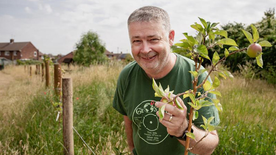 Volunteer posing for photo with young tree in grassy field.